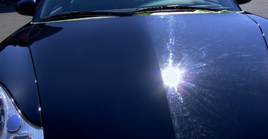 A deep blue car hood polished to a mirror finish with a sharp starburst reflection of the sun.